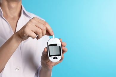 Photo of Female doctor holding digital glucometer on color background, closeup view with space for text. Medical object