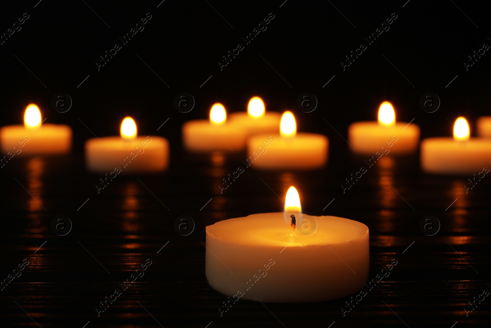 Photo of Burning candle on black table against blurred background, space for text