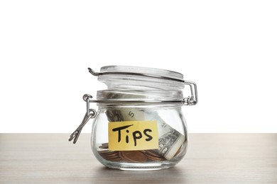 Tip jar with money on wooden table against white background