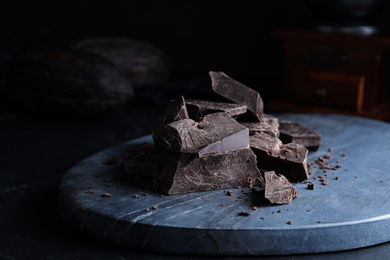 Photo of Pieces of tasty dark chocolate on grey marble board, closeup