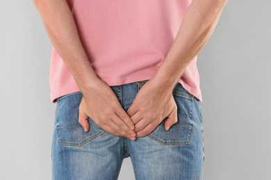 Photo of Man suffering from hemorrhoid on light grey background, closeup