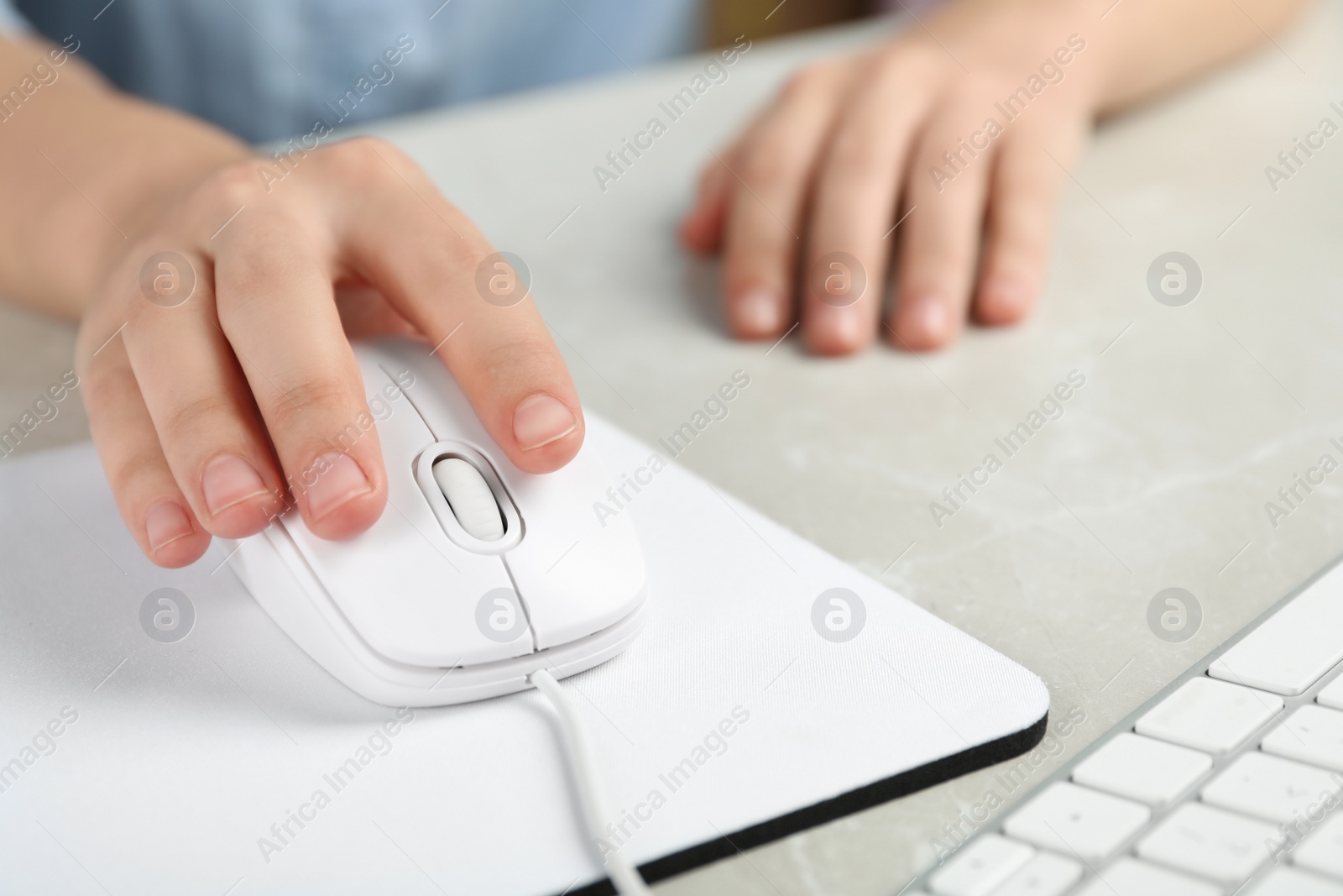 Photo of Woman using wired computer mouse on pad at light grey marble table, closeup