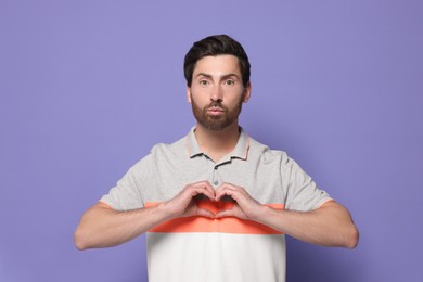 Photo of Handsome man making heart with hands and blowing kiss on violet background