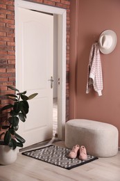 Hallway interior with beautiful houseplant, soft ottoman and door mat on floor near entrance