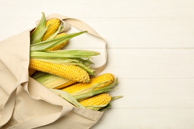 Photo of Corn cobs in bag on white wooden table, flat lay. Space for text