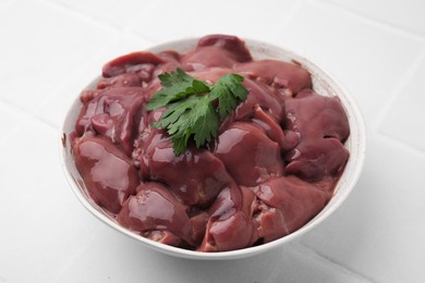 Bowl of raw chicken liver with parsley on white tiled table, closeup