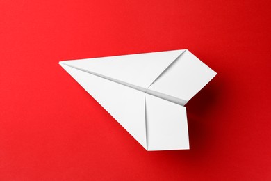 Photo of Handmade white paper plane on red background, top view