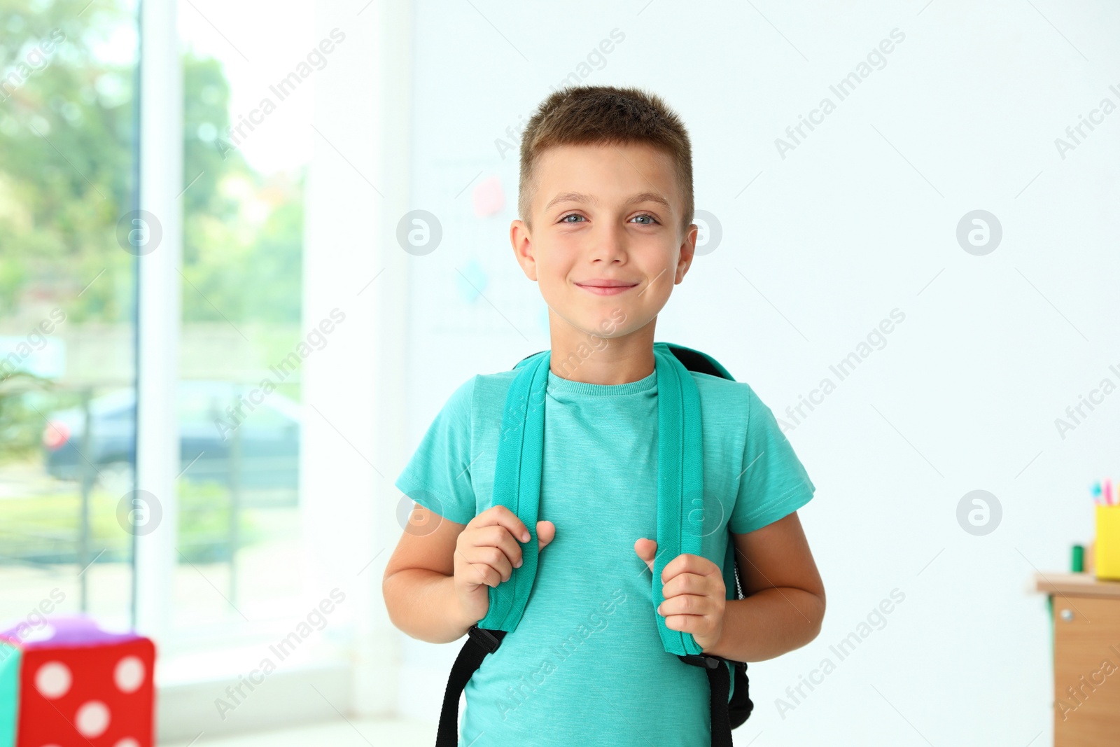 Photo of Cute little boy with backpack in classroom at school