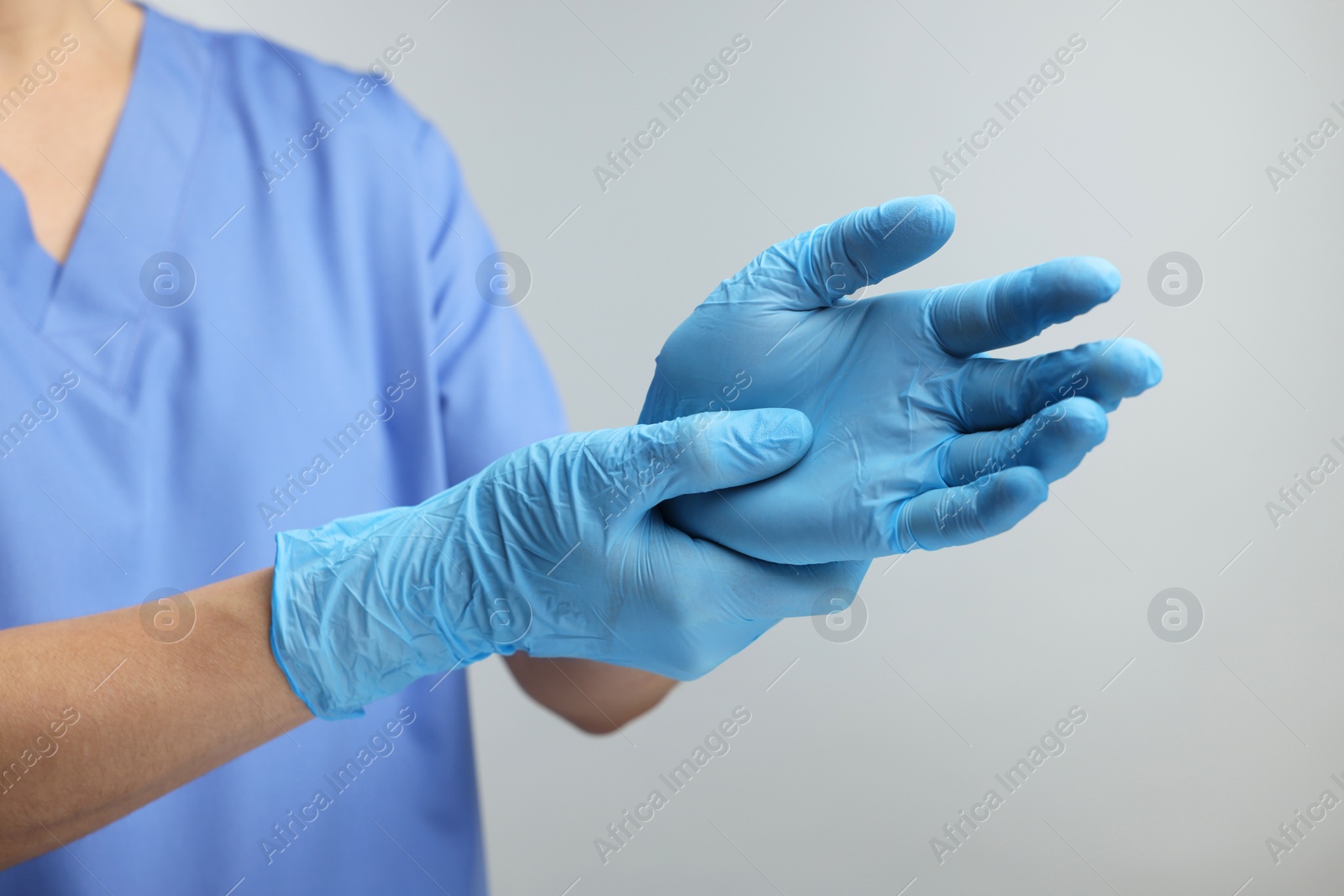 Photo of Doctor wearing light blue medical gloves on grey background, closeup