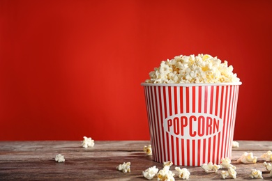 Photo of Bucket of tasty popcorn on table against red background, space for text. Watching cinema