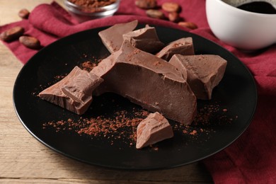 Photo of Pieces of tasty milk chocolate and cocoa powder on wooden table, closeup