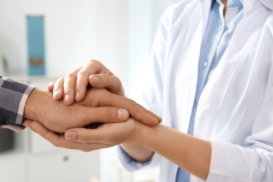 Female doctor comforting man on blurred background, closeup of hands. Help and support concept