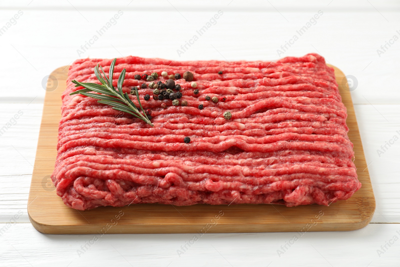 Photo of Raw ground meat, rosemary and peppercorns on white wooden table