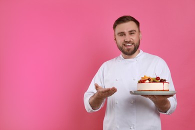 Happy professional confectioner in uniform holding delicious cake on pink background. Space for text