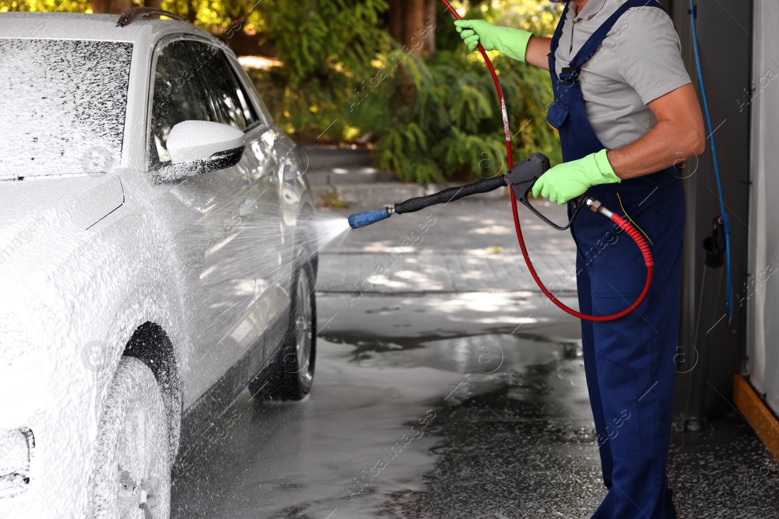 Photo of Worker washing auto with high pressure water jet at outdoor car wash, closeup