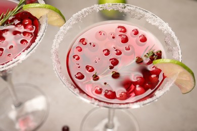 Tasty cranberry cocktail with rosemary and lime in glasses on grey table, closeup