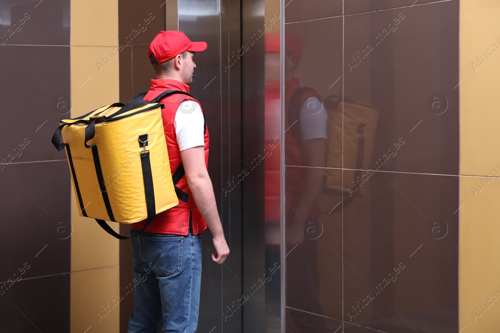 Photo of Male courier with thermo bag waiting for elevator. Food delivery service