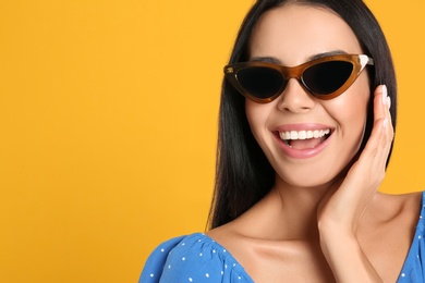 Photo of Beautiful woman wearing sunglasses on yellow background, closeup. Space for text