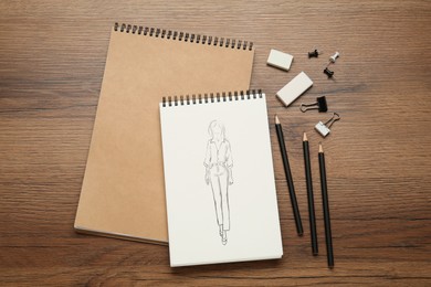 Image of Sketch of stylish clothes in pad on wooden table. Fashion designer's desk with stationery, flat lay