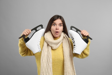 Emotional woman with ice skates on light grey background