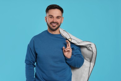 Photo of Man holding garment cover with clothes on light blue background. Dry-cleaning service