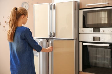 Photo of Young woman opening refrigerator doors in kitchen