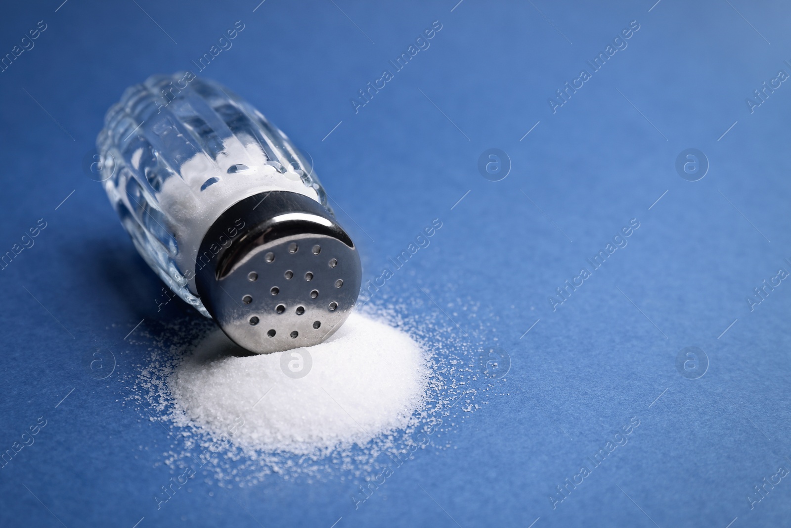 Photo of Scattered salt and shaker on blue background, closeup. Space for text