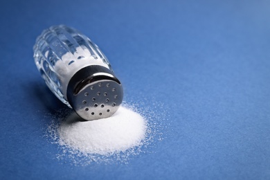 Photo of Scattered salt and shaker on blue background, closeup. Space for text