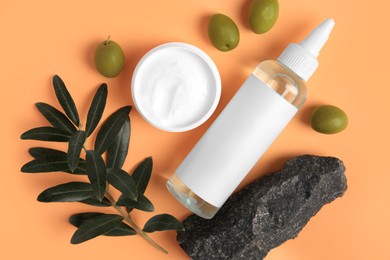 Flat lay composition with different cosmetic products and olives on pale orange background