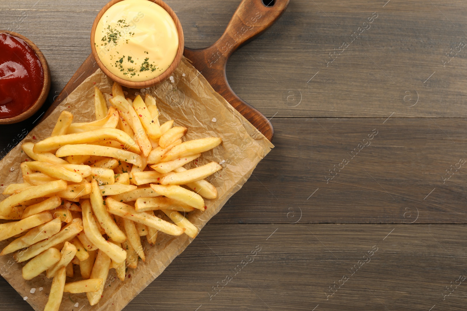 Photo of Delicious french fries served with sauces on wooden table, flat lay. Space for text