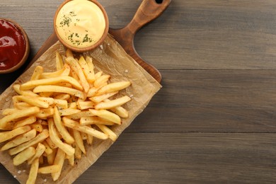 Delicious french fries served with sauces on wooden table, flat lay. Space for text