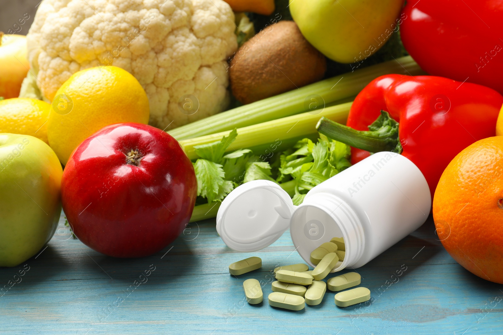 Photo of Dietary supplements. Overturned bottle with pills near food products on light blue wooden table