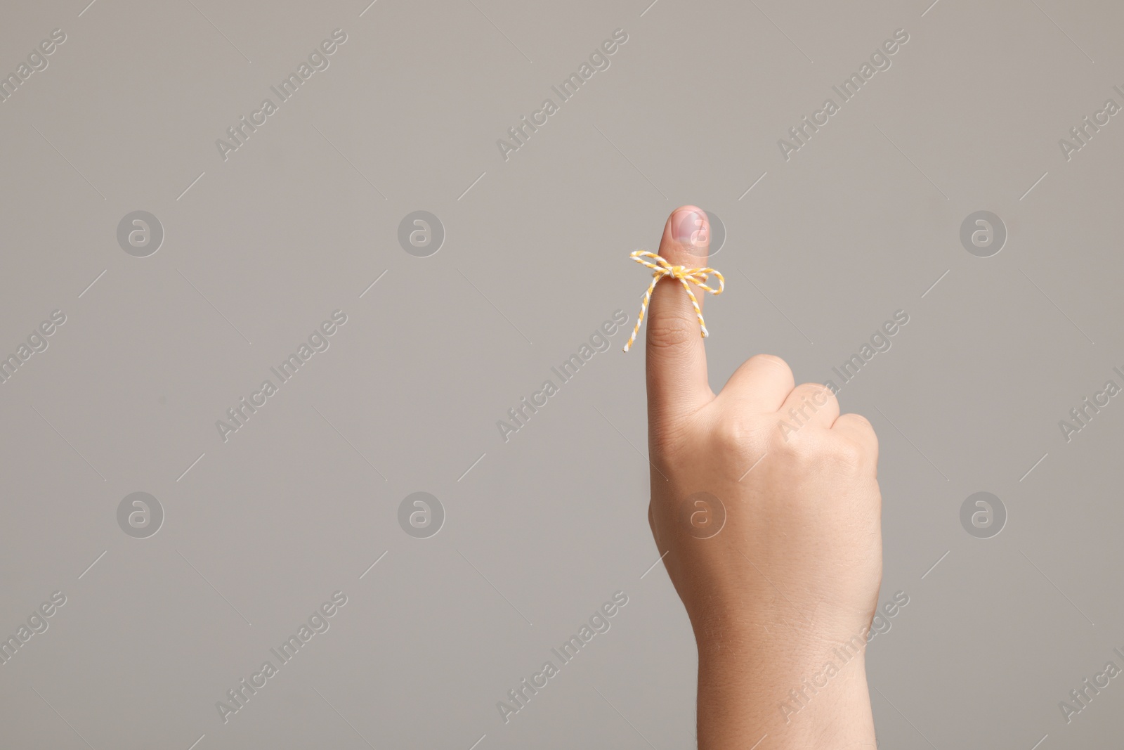 Photo of Man showing index finger with tied bow as reminder on light grey background, closeup. Space for text