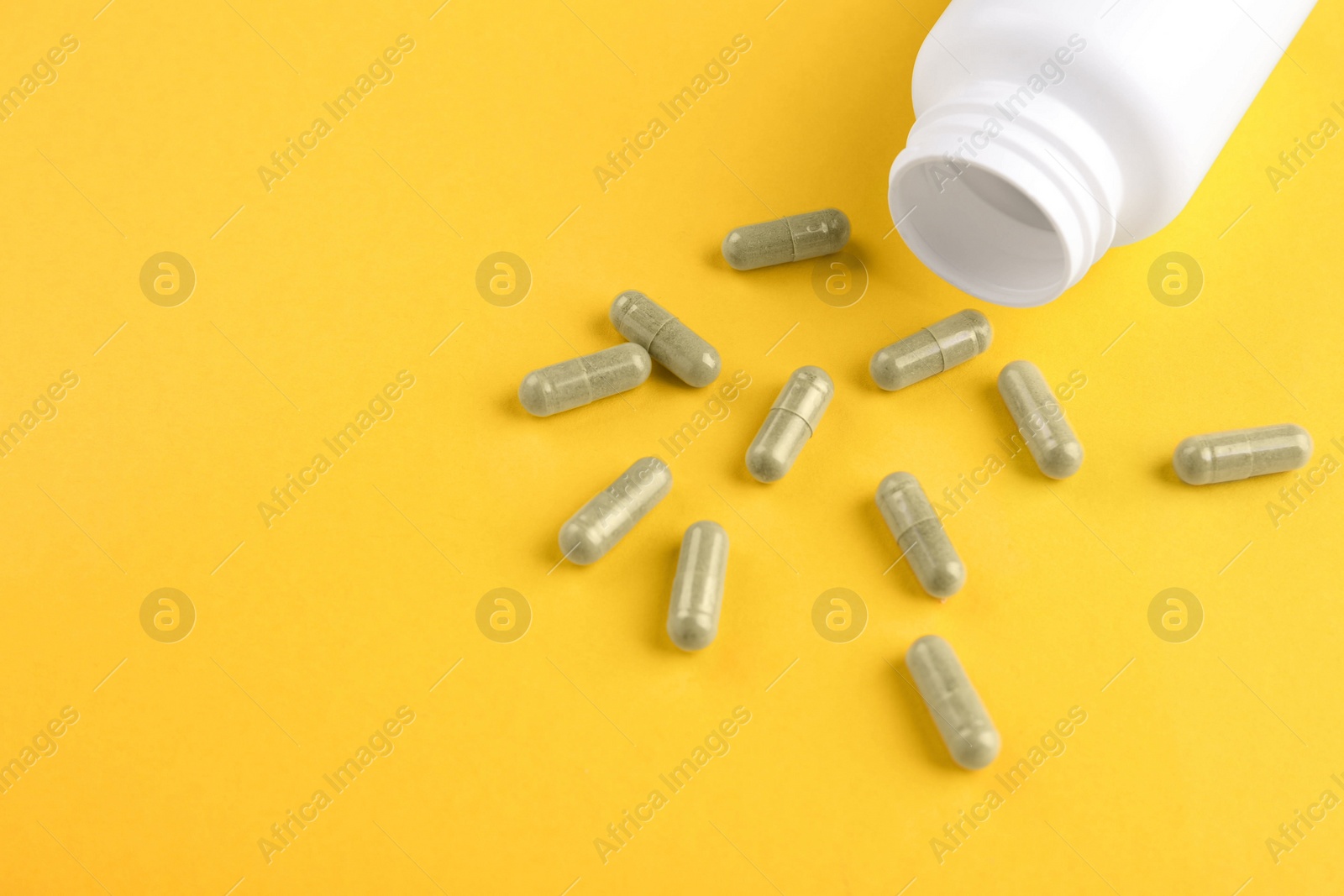 Photo of Bottle and vitamin capsules on yellow background, closeup. Space for text