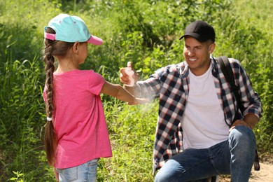 Photo of Father spraying tick repellent on his little daughter's arm during hike in nature