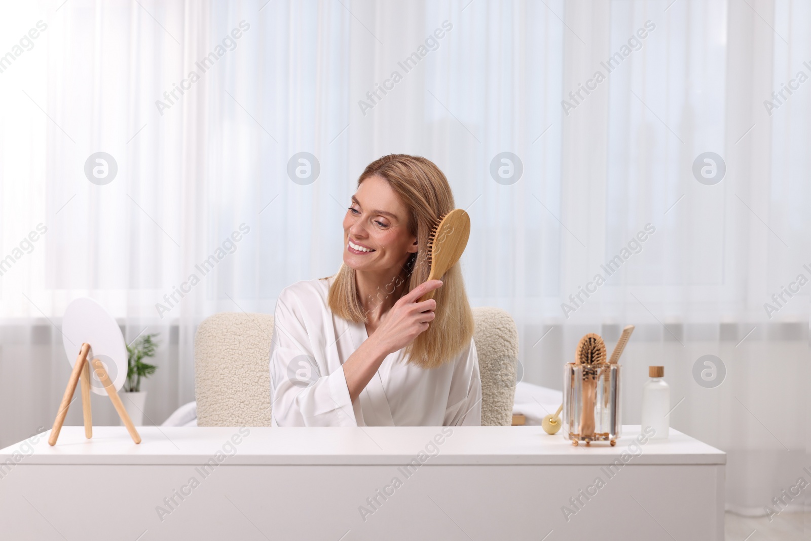 Photo of Beautiful woman brushing her hair at vanity in bedroom