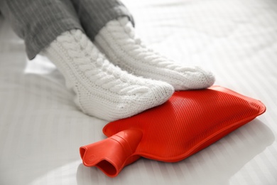 Photo of Person warming feet with hot water bottle on bed, closeup