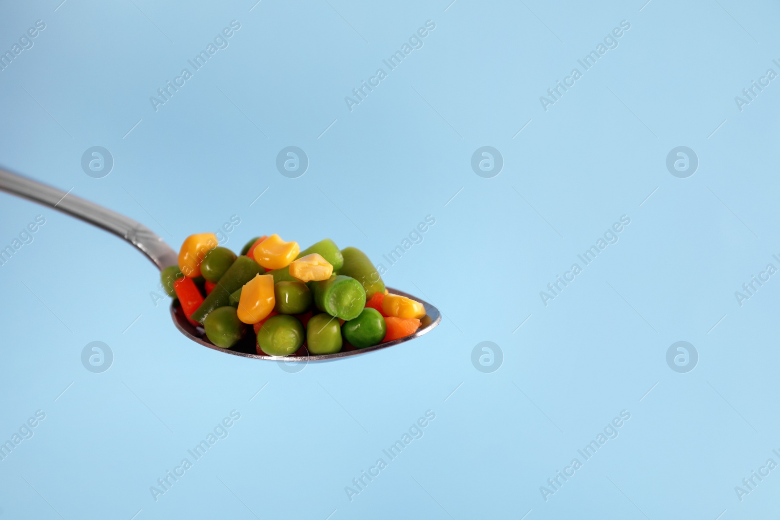 Photo of Fresh vegetables in spoon on light blue background. Space for text