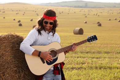 Photo of Hippie man playing guitar near hay bale in field