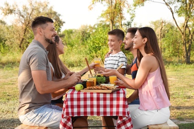 Happy young people and little boy having picnic at table in park