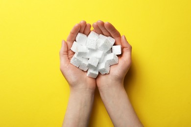 Photo of Woman with handful of styrofoam cubes on yellow background, top view