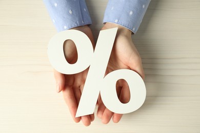 Photo of Woman holding percent sign at white wooden table, top view