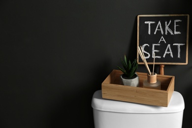 Photo of Decor elements and toilet bowl near black wall, space for text. Bathroom interior