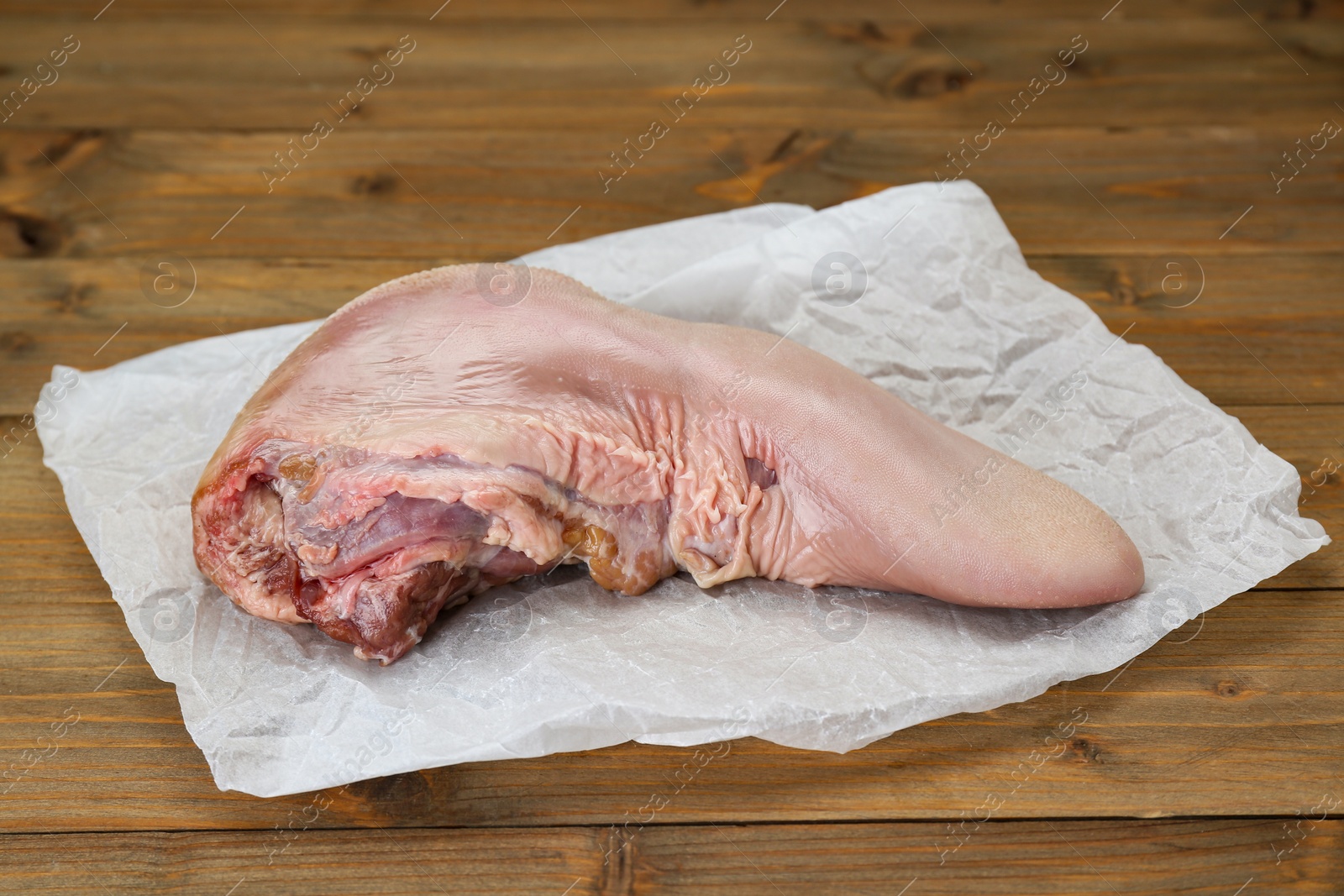 Photo of Parchment with raw beef tongue on wooden table, closeup