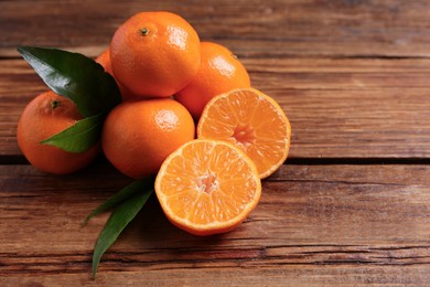 Photo of Fresh tangerines with green leaves on wooden table, space for text