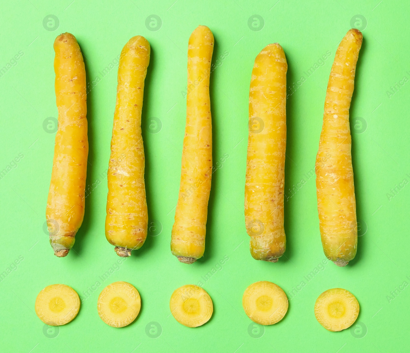 Photo of Whole and cut raw yellow carrots on green background, flat lay