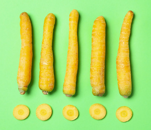 Whole and cut raw yellow carrots on green background, flat lay