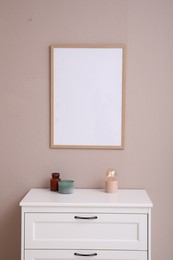 Photo of Empty frame hanging on pale rose wall over chest of drawers in room. Mockup for design