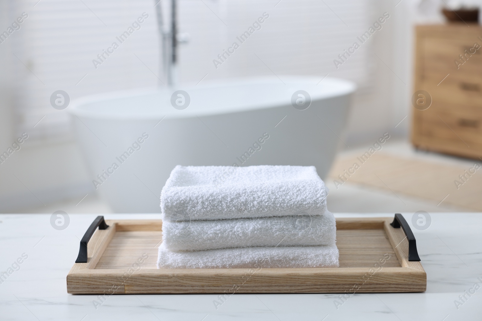 Photo of Wooden tray with stacked bath towels on white table in bathroom
