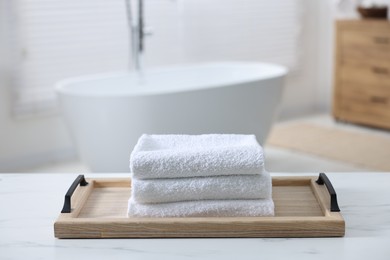 Photo of Wooden tray with stacked bath towels on white table in bathroom